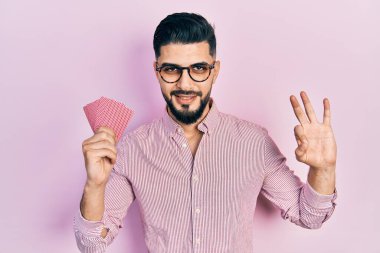 Poker kartları tutan yakışıklı adam parmaklarıyla imza atıyor, gülümsüyor ve mükemmel bir sembol. 