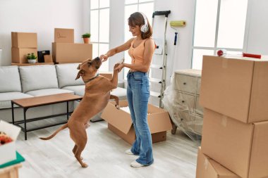 Beyaz bir kadın, kendinden emin bir şekilde gülümsüyor müzik dinliyor ve evde köpekle dans ediyor.