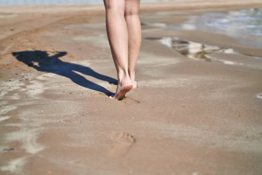 Genç İspanyol kadın deniz kenarında kumda yürüyor.