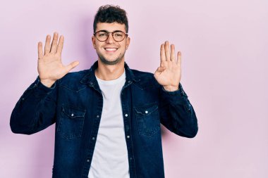 Gündelik kıyafetler giyen ve gözlük takan İspanyol genç adam dokuz numarayı gösterip işaret ederken kendinden emin ve mutlu bir şekilde gülümsüyor.. 