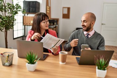 Ofiste bilgisayar ve akıllı telefon kullanarak çalışırken gülümseyen iki İspanyol iş adamı..
