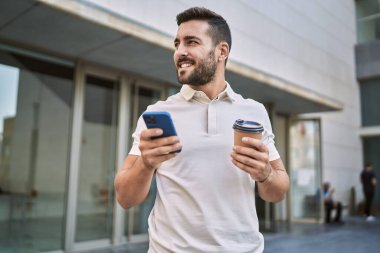 Genç İspanyol adam akıllı telefon kullanıyor, sokakta kahve içiyor.