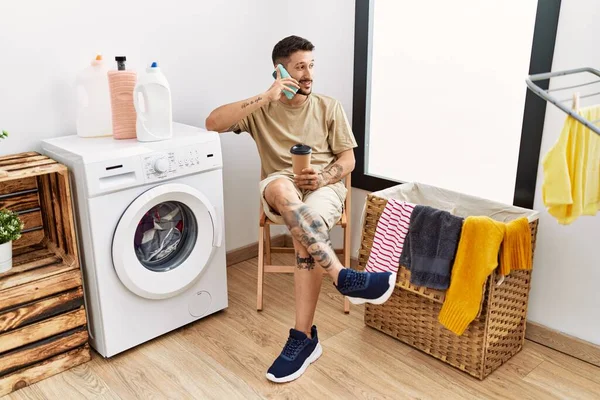Young Hispanic Man Waiting Washing Machine Speaking Phone Laundry Room — Fotografia de Stock