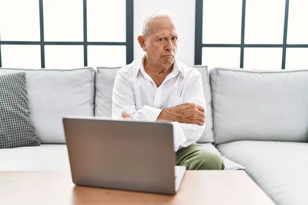 ソファの上に座っている自宅でノートパソコンを使用しているシニア男性は懐疑的で緊張し 両腕を組んで顔に不承認式 否定的な人 — ストック写真