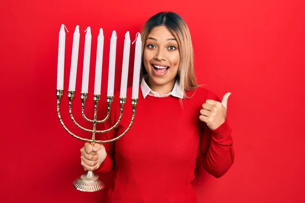 Beautiful Hispanic Woman Holding Menorah Hanukkah Jewish Candle Pointing Thumb — Stock Photo, Image