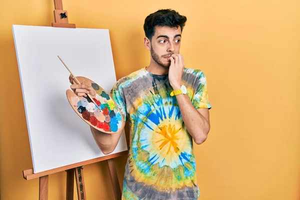 画家のイーゼルスタンドでパレットで描画立っている若いヒスパニック系の男は 口の爪をかむ上で手でストレスや緊張している 不安の問題 — ストック写真