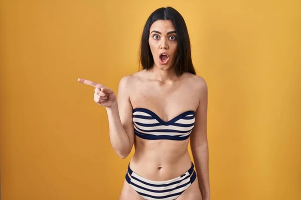 Joven Morena Con Bikini Sobre Fondo Amarillo Sorprendida Señalando Con — Foto de Stock