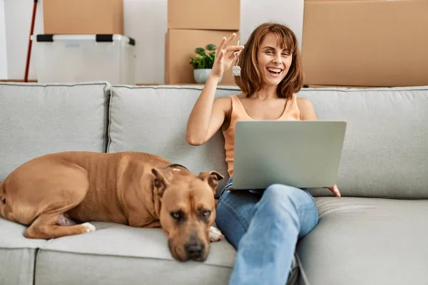 Young caucasian woman having video call and holding key sitting on sofa with dog at home