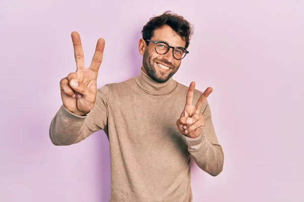 Pohledný Muž Vousy Roláku Svetru Brýlích Usmívající Kameru Ukazující Prsty — Stock fotografie
