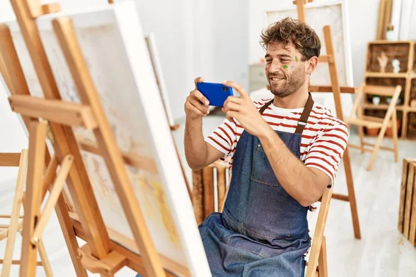 Young hispanic man make photo to draw using smartphone at art studio