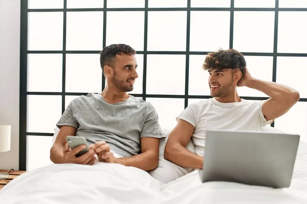 Dos Hombres Hispanos Pareja Usando Laptop Smartphone Sentados Cama Dormitorio —  Fotos de Stock