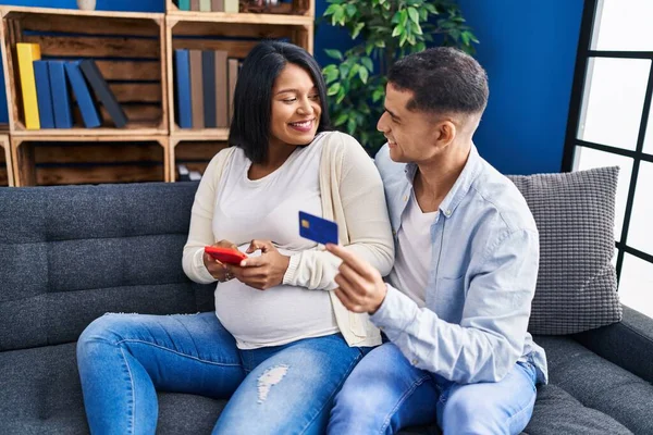 若いラテンカップル期待赤ちゃん使用スマートフォンとクレジットカードで自宅 — ストック写真