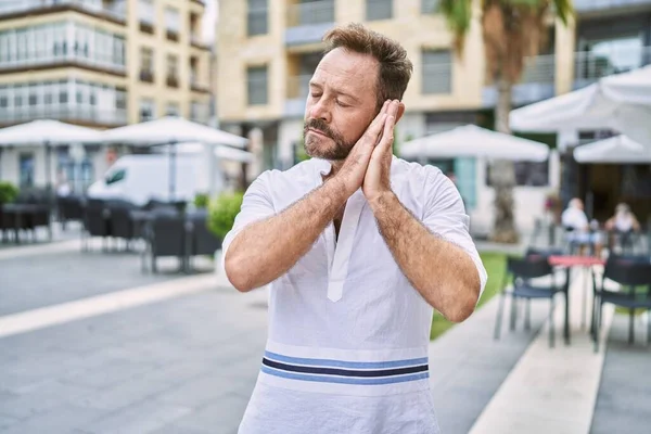 Middle age man outdoor at the city sleeping tired dreaming and posing with hands together while smiling with closed eyes.