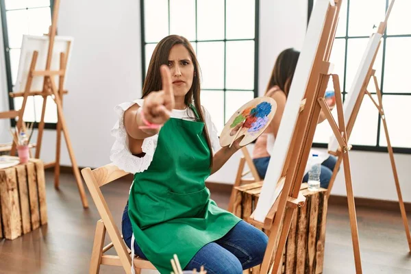 Young Hispanic Artist Women Painting Canvas Art Studio Pointing Finger — Zdjęcie stockowe