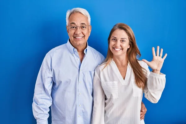 Middelbare Leeftijd Hispanic Paar Staan Blauwe Achtergrond Tonen Wijzen Met — Stockfoto