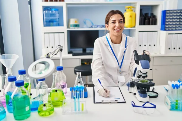 Mujer Hispana Joven Vistiendo Uniforme Científico Usando Microscopio Escritura Portapapeles — Foto de Stock
