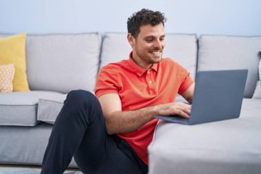 Genç İspanyol adam evde dizüstü bilgisayar kullanıyor.
