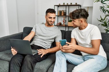 Evde akıllı telefon ve dizüstü bilgisayar kullanan iki İspanyol erkek.