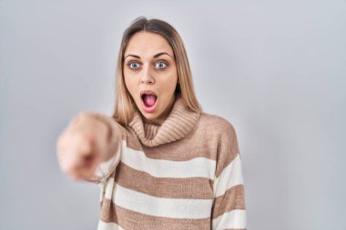 Sarışın, balıkçı yaka kazak giyen genç bir kadın izole edilmiş arka planda parmağı önde, ağzı açık, şaşırmış, ön tarafta bir şey var. 