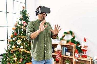 VR gözlük takan genç İspanyol adam Noel ağacının yanında duruyor.