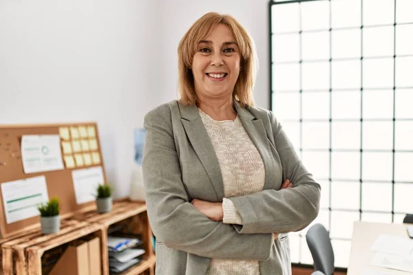 Middle age businesswoman smiling happy standing with arms crossed gesture at the office.