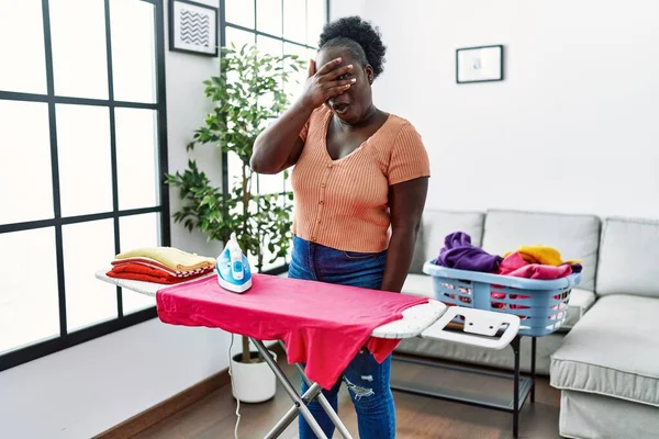 Young African Woman Ironing Clothes Home Peeking Shock Covering Face — Stockfoto