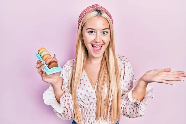 Menina Loira Jovem Segurando Deliciosos Doces Macarons Comemorando Realização Com — Fotografia de Stock