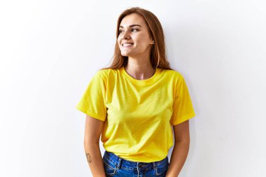 Genç esmer kadın izole edilmiş arka planda duruyor. Yüzünde gülümseme, doğal bir ifade ile yan yana bakıyor. Kendinden emin gülen. 