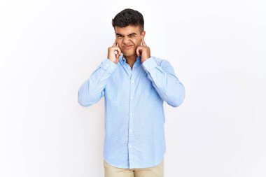 İzole edilmiş arka planda duran İspanyol gömlekli genç adam yüksek sesli müzik sesi için kulakları parmaklarıyla kapatıyor. sağır kavramı. 