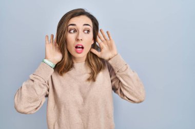 Young woman standing over isolated background trying to hear both hands on ear gesture, curious for gossip. hearing problem, deaf 