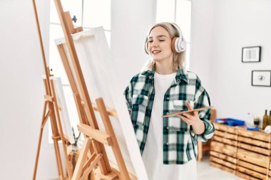 Sanat stüdyosunda resim yaparken ve müzik dinlerken gülümseyen genç sanatçı kız..