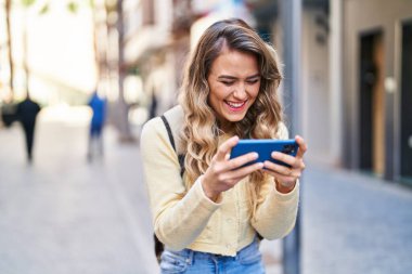Genç bayan turist gülümsüyor. Sokakta akıllı telefondan videolar izliyor.