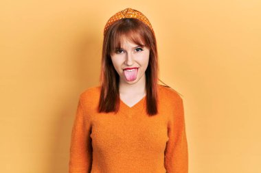 Kızıl saçlı, turuncu süveter giyen genç bir kadın komik bir ifadeyle dilini dışarı çıkartıyor. duygu kavramı. 