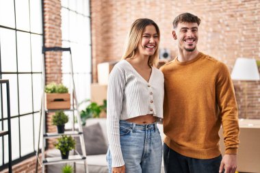 Genç adam ve kadın çift yeni evlerinde birbirlerine sarılıyorlar.