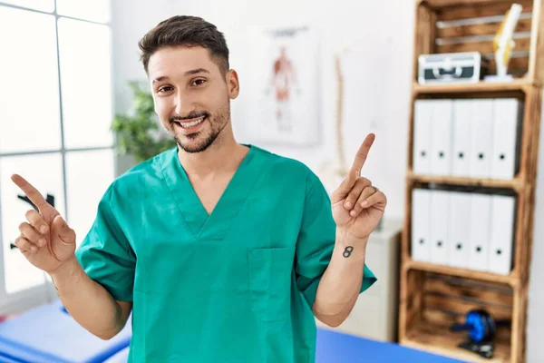 Young Physiotherapist Man Working Pain Recovery Clinic Smiling Confident Pointing — Stockfoto
