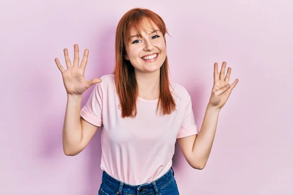 红头发的年轻女人穿着休闲的粉色T恤 手指着9号 面带微笑 自信而快乐 — 图库照片