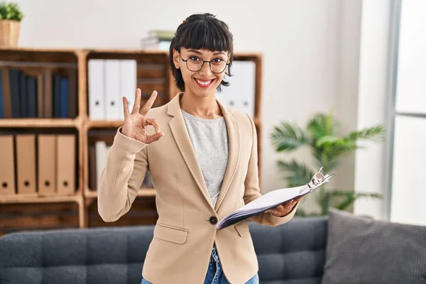 在会客室工作的年轻惊慌失措的女人用手指签了名 微笑着表示友善的手势 是个很好的象征 — 图库照片