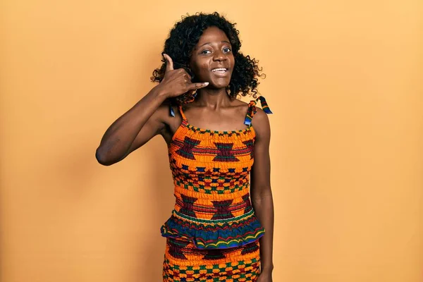 若いアフリカ系アメリカ人の女性は 伝統的なアフリカの服を着て 電話で話すような手と指で携帯電話のジェスチャーをして笑っています コミュニケーションの概念 — ストック写真