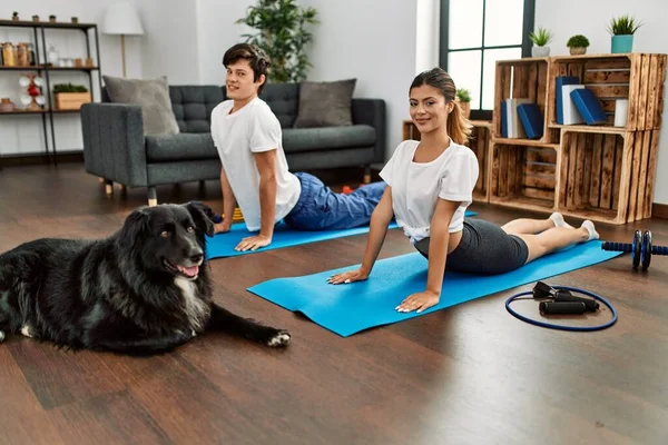 一对年轻的高加索夫妇笑着高兴地在家里用狗训练瑜伽 — 图库照片