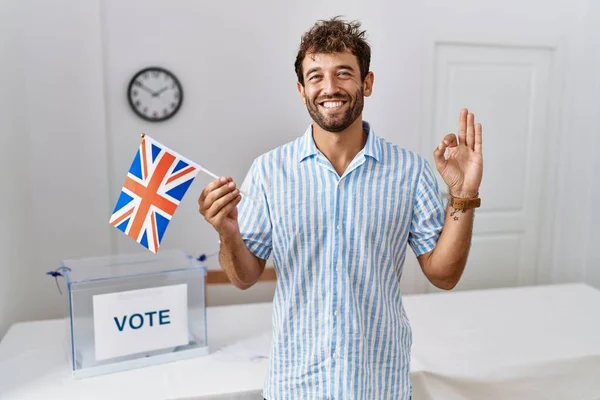 英俊潇洒的年轻人在选战中举着英国国旗 用手指做手势 微笑友善地表示出优秀的象征 — 图库照片