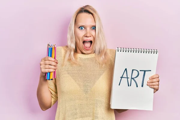 美しいですCaucasianブロンド女性保持アートノートと色鉛筆祝うクレイジーと驚きのために成功でオープン目叫んで興奮 — ストック写真