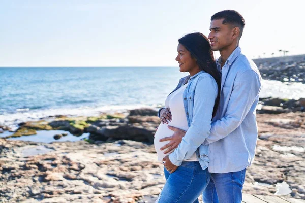 Young Latin Couple Expecting Baby Hugging Each Other Standing Seaside — Stockfoto