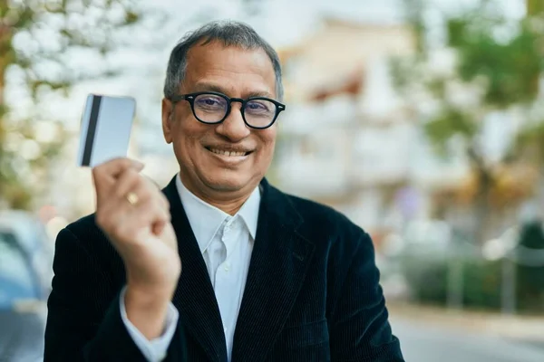 Middle age southeast asian man standing and smiling confident holding credit card at the city