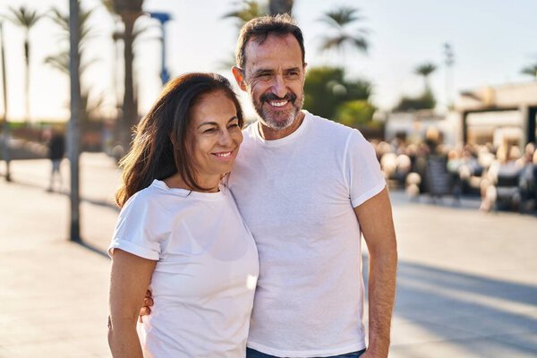 Middle age man and woman couple hugging each other standing at street