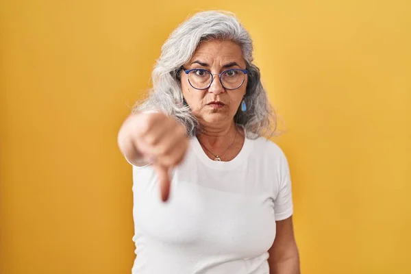 白髪の中年女性が黄色の背景の上に立ち 親指を下にジェスチャーで拒絶と否定を示す不満と怒りを見ています 悪い表現 — ストック写真