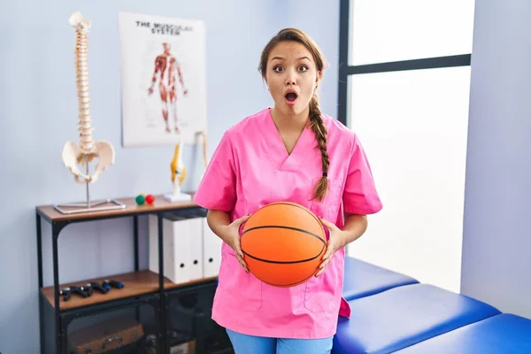 Young Hispanic Woman Working Physiotherapy Clinic Holding Basketball Ball Afraid — Stock Photo, Image