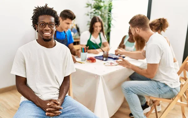 Group of people drawing sitting on the table. African american man smiling happy looking to the camera at art studio.