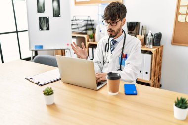 Genç İspanyol doktor klinikte bilgisayarla video görüşmesi yapıyor.