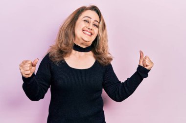 Orta yaşlı beyaz kadın, başarı için heyecanlı, kolları havada, gözleri kapalı zafer kutlamaları yaparken gülümsüyor. Kazanan konsept. 