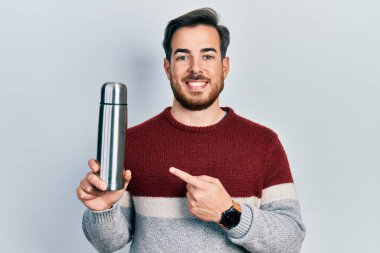 Sakallı, yakışıklı, beyaz bir adam. Termo tutuyor. Gülümsüyor. 